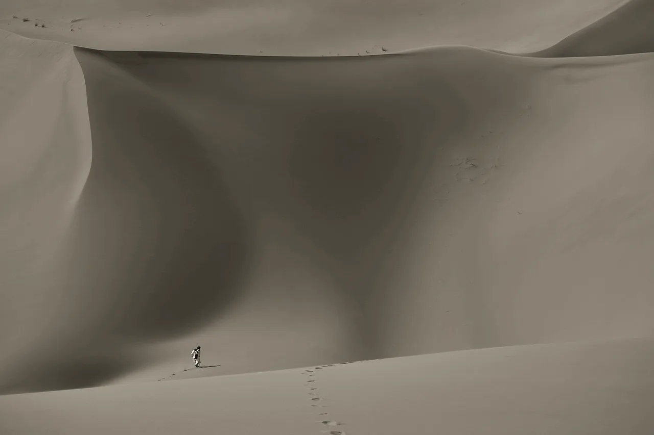 A lone figure walking a vast desert dune, tiny against the sand